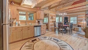 A rustic cabin interior with wooden walls, a kitchen with wooden cabinets, a dining area with a table and chairs, and a chandelier. - Bear Den-Mountain Log Cabin, Wood Fireplace, Pool Table, Gas Grill (Seven Devils)