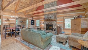 A log cabin interior with a stone fireplace, wooden furniture, and a high ceiling with exposed beams. - Bear Den-Mountain Log Cabin, Wood Fireplace, Pool Table, Gas Grill (Seven Devils)