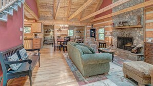 A log cabin interior with a stone fireplace, wooden beams, and a cozy seating area. - Bear Den-Mountain Log Cabin, Wood Fireplace, Pool Table, Gas Grill (Seven Devils)