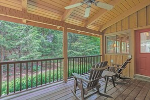 A wooden porch with a ceiling fan, two Adirondack chairs, and a view of a forested area. - Bear Den-Mountain Log Cabin, Wood Fireplace, Pool Table, Gas Grill (Seven Devils)