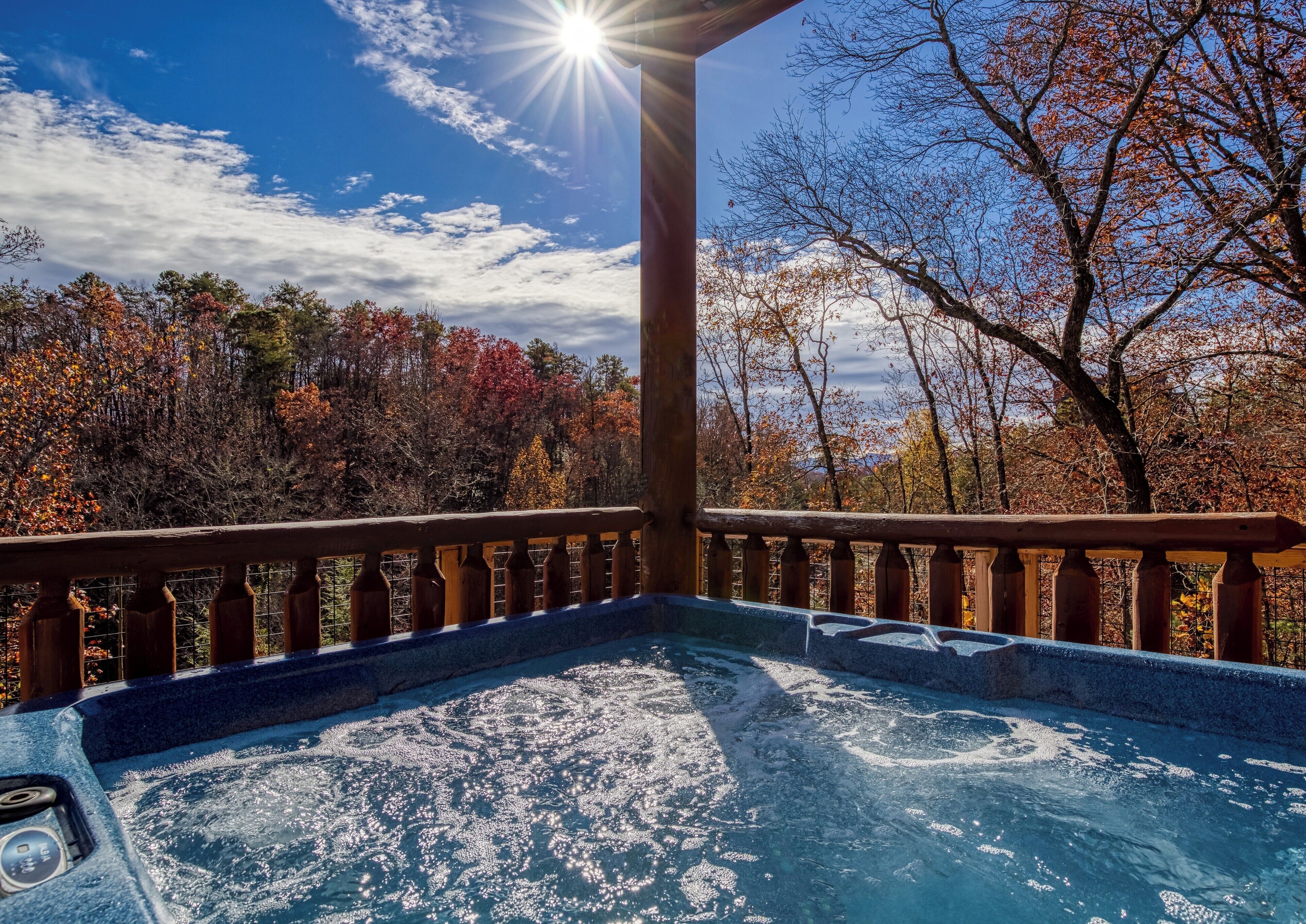 A hot tub with a wooden deck and railing, surrounded by autumn foliage and a clear sky.