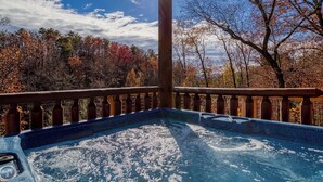 Ein Whirlpool mit Holzterrasse und Geländer, umgeben von Herbstlaub und blauem Himmel.