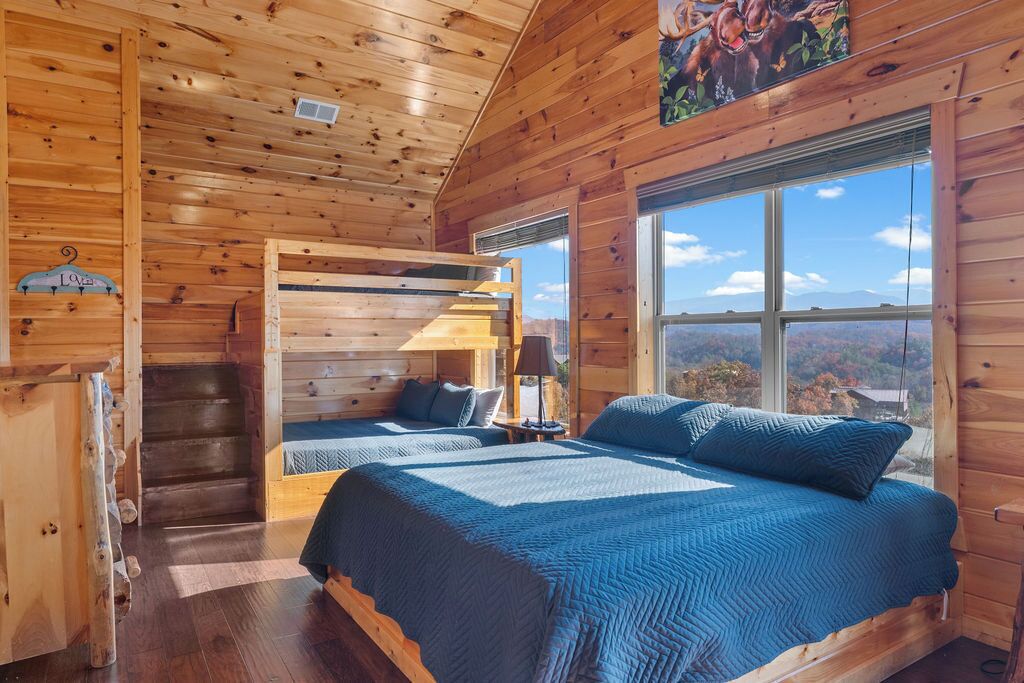 A wooden cabin bedroom with two beds, a window with a mountain view, and a ladder leading to a loft area.