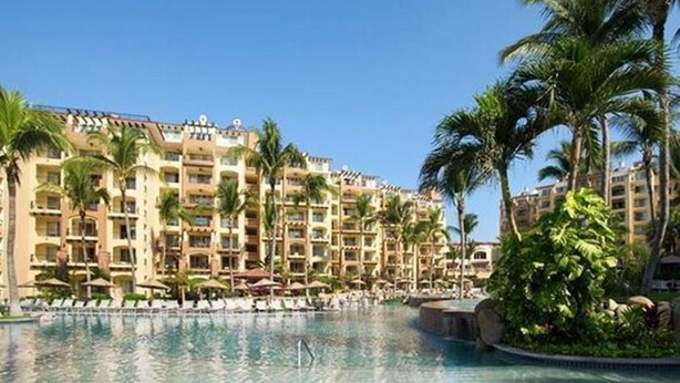 A resort with a large pool, palm trees, and multi-story buildings. - Christmas in paradise (Nuevo Vallarta)