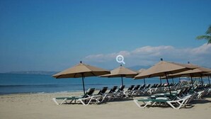 A beach with rows of sun loungers under umbrellas, a clear sky, and the ocean in the background. - Christmas in paradise (Nuevo Vallarta)