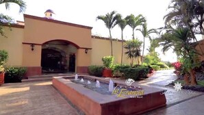A hotel entrance with a fountain, palm trees, and a clear sky. - Christmas in paradise (Nuevo Vallarta)
