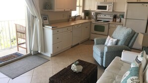 A modern kitchen with white cabinets, a microwave, and a stove. There is a wicker ottoman with a pineapple decoration. - Amazing one bedroom direct ocean front condo with beautiful view of the ocean! (COCOA BEACH)