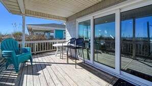 A covered outdoor deck with a table and chairs, large sliding glass doors, and a view of the beach. - SeaClusion South - Oceanfront - Dog Friendly (Topsail Beach)