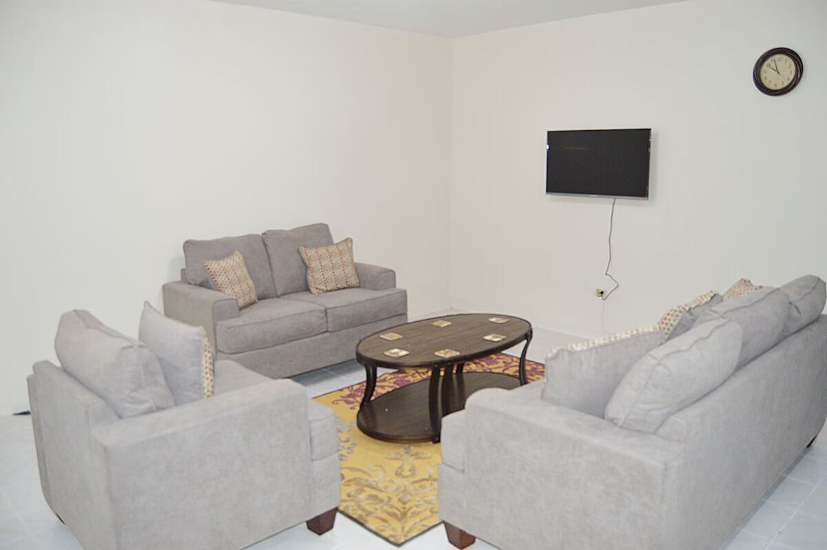 A living room with a grey sofa set, a coffee table, and a flat-screen TV mounted on the wall.
