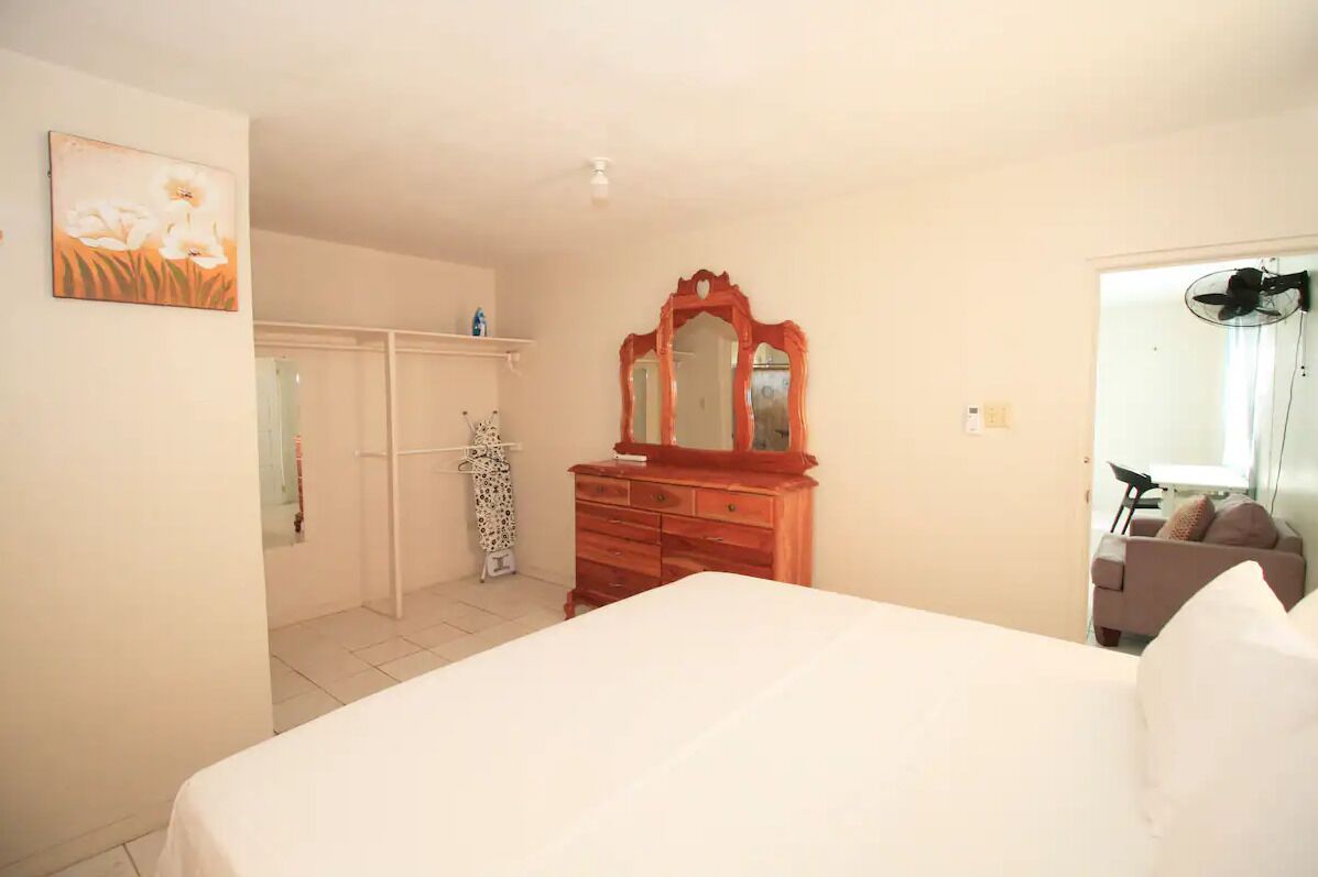 Um quarto com uma cama, cômoda de madeira, espelho e guarda-roupa.