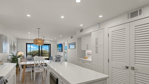 A modern kitchen with white cabinetry, a central island, and a dining area with chairs.