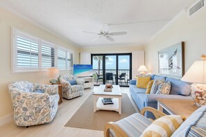 A spacious living room with a large window, a ceiling fan, and a view of the ocean. - OCEAN'S REACH 3D2: 2-Bdrm, 2nd Floor/Corner Unit, Beautiful Gulf Views! (Sanibel Island)