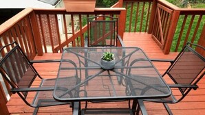 Eine Terrasse mit einem quadratischen Tisch und vier Stühlen, umgeben von einem Holgitter.
