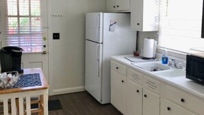 Eine kleine Küche mit weißen Schränken, einem Kühlschrank, einer Mikrowelle und einem Spülbecken.