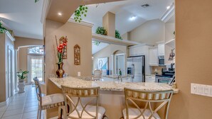 A kitchen with a central island, two bar stools, and a decorative vase. - Electric heated pool | BBQ | Pet Friendly (Cape Coral)