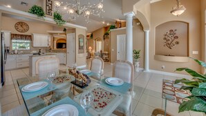 A spacious dining area with a glass table, white chairs, and a chandelier. - Electric heated pool | BBQ | Pet Friendly (Cape Coral)