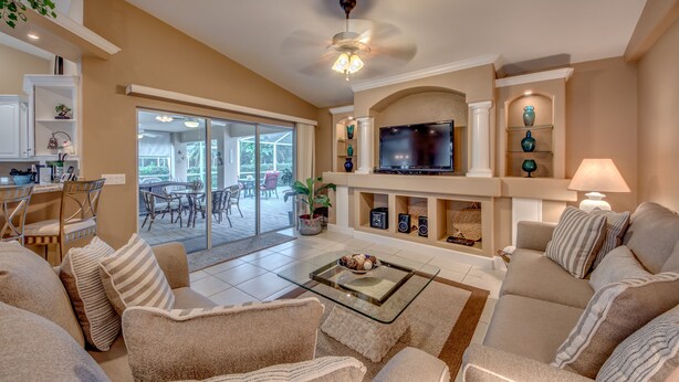 A spacious living room with a glass coffee table, beige sofas, a flat-screen TV, and a fireplace. - Electric heated pool | BBQ | Pet Friendly (Cape Coral)