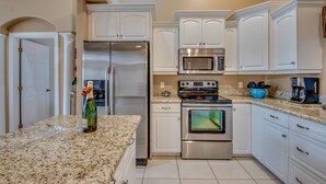A modern kitchen with white cabinets, stainless steel appliances, and a granite countertop. - Electric heated pool | BBQ | Pet Friendly (Cape Coral)