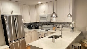 Una cocina moderna con armarios blancos, electrodomésticos de acero inoxidable, una isla central con taburetes y luces colgantes.