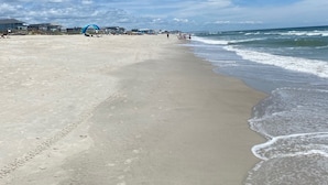 Una playa con cielo despejado, orilla de arena y algunos edificios al fondo.