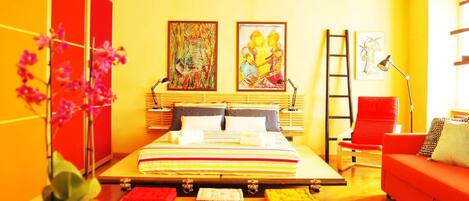 Une chambre moderne avec un grand lit, un canapé rouge et deux tableaux accrochés au mur.