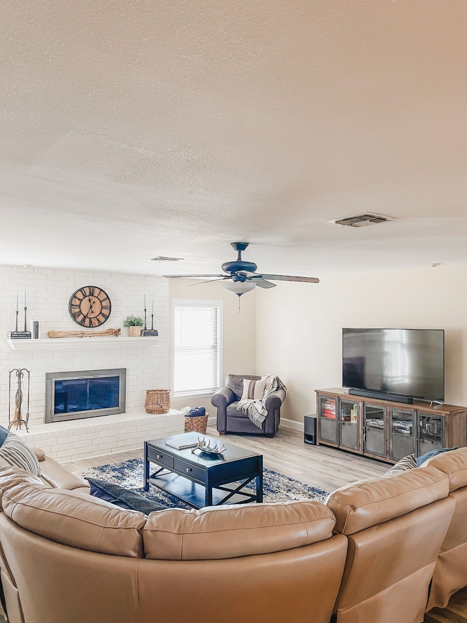 A living room with a beige sofa, a fireplace, a television, and a ceiling fan.