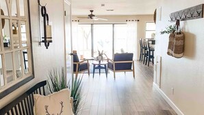 Ein großzügiges Wohnzimmer mit Holzboden, einer schwarzen Couch mit Zierkissen, einem Deckenventilator und einem Essbereich mit Stühlen und Tisch.