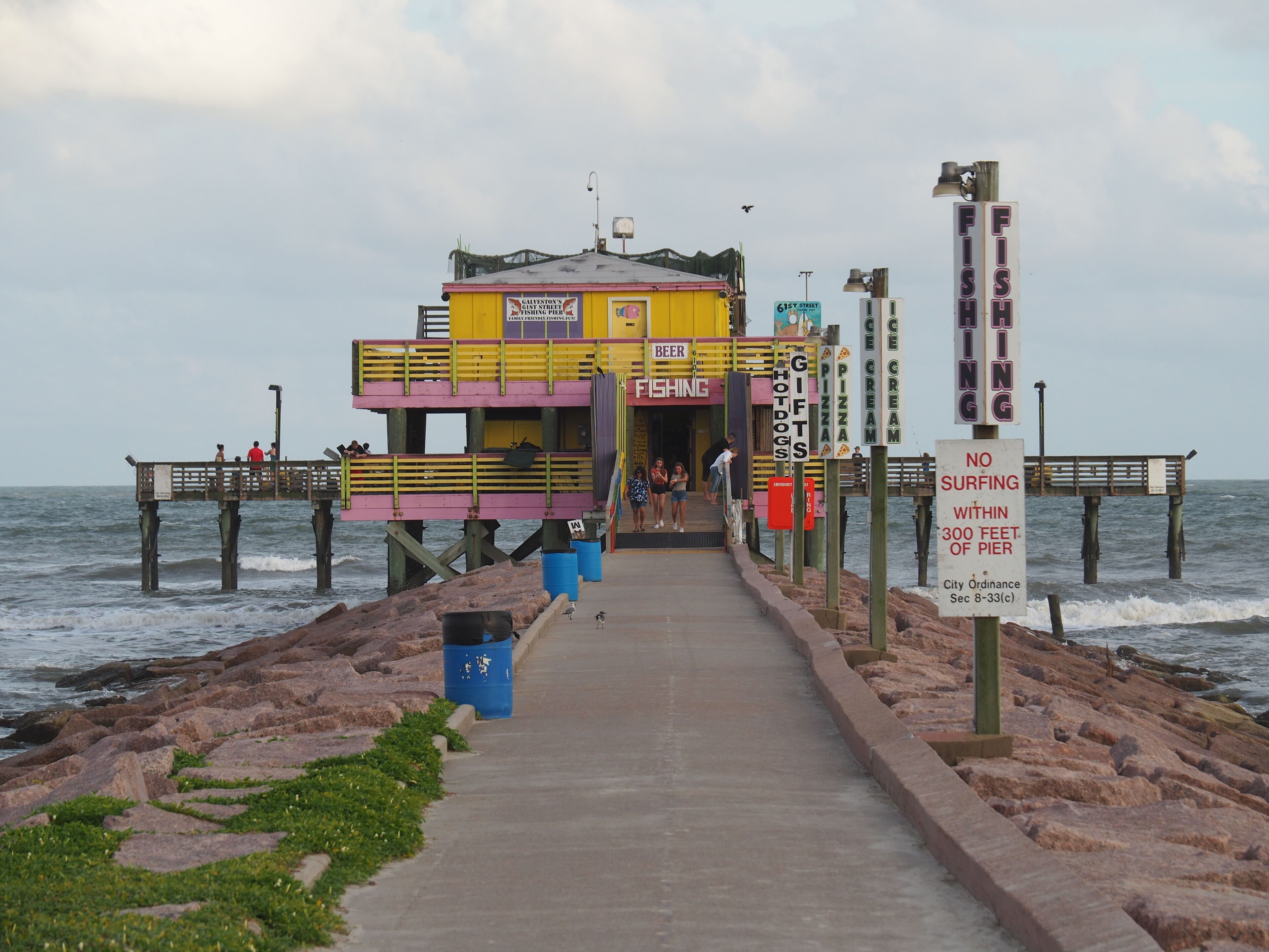 A pier with a colorful building offering beer, fishing, pizza, and ice cream.