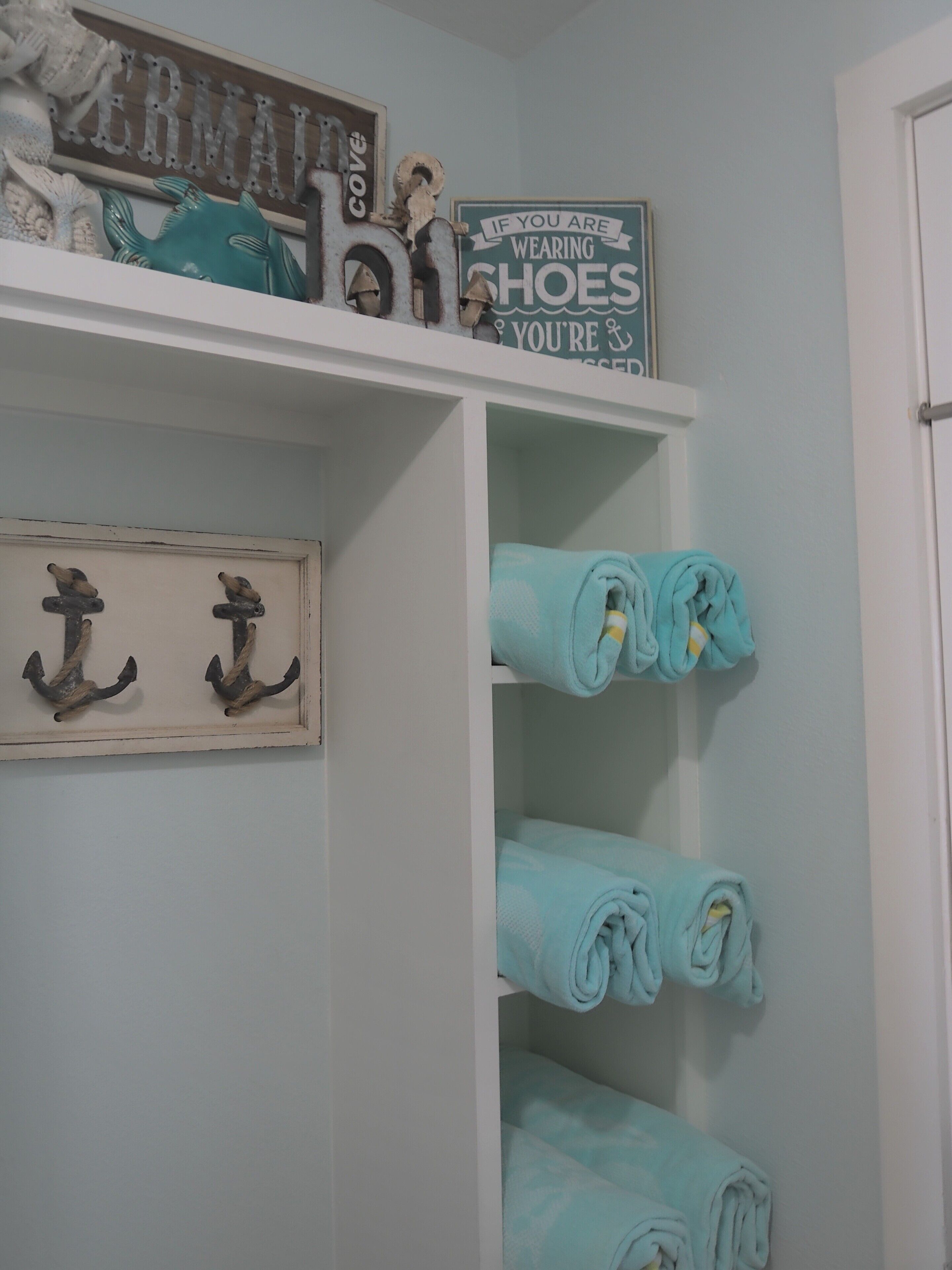 A bathroom with a white shelf holding towels and decorative items.