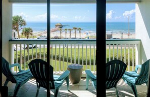 A balcony with two chairs and a trash can, overlooking a beach with palm trees and a pier. - Amazing Front Facing Top Floor with unobstructed Gulf and Beach View!! #302 (Galveston)