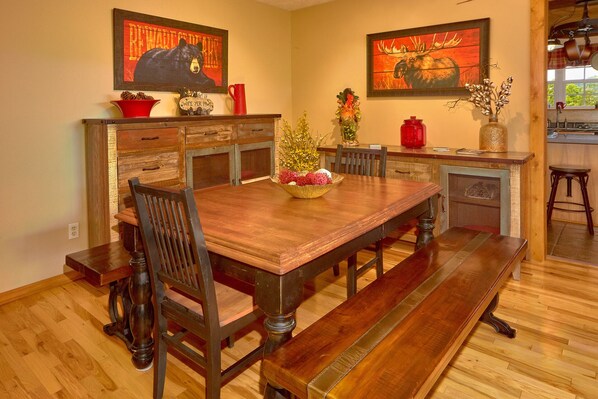 A dining area with a wooden table, chairs, and a bench. There are two paintings on the walls, a red mug, and a vase with flowers on the table. - Above it All | Views, Loft, Near Pigeon Forge! (Sevierville)