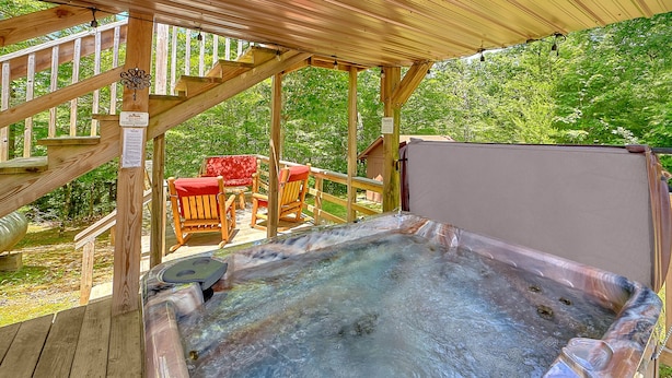Un bain à remous sous une pergola en bois, avec une terrasse en bois et des chaises rouges.