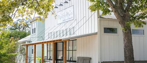 A building with a sign reading "Pigs Fly & Co. boutique and merchandise" and a wooden porch with chairs.