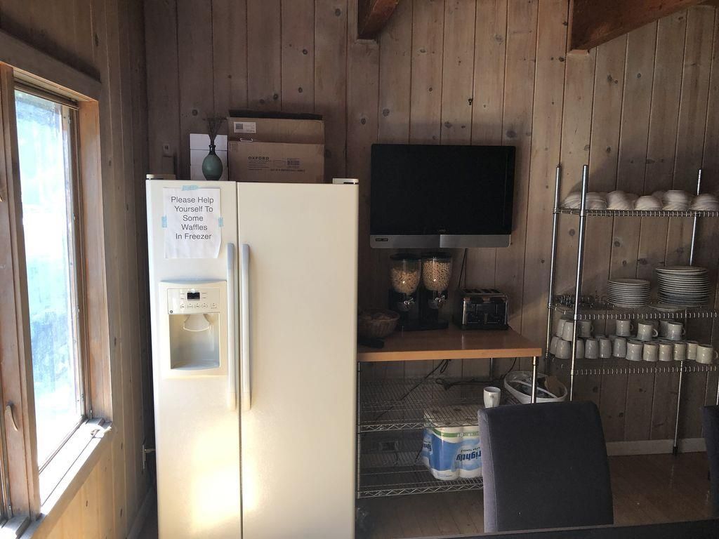 A kitchen with a refrigerator, a television, and a shelf with plates and cups.