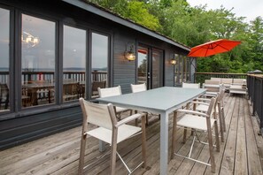 Eine Terrasss mit Tisch und Stühlen, großen Fenstern und einem roten Sonnenschirm.