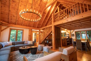 A spacious wooden interior with a high ceiling, a staircase leading to an upper level, and a cozy seating area with sofas and a coffee table.