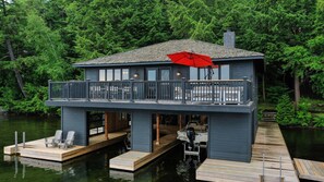 A waterfront house with a balcony, dock, and a red umbrella.