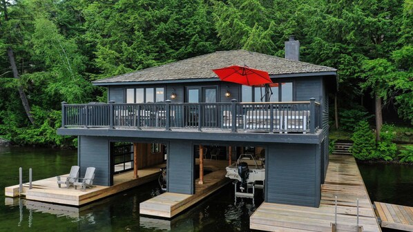 A waterfront house with a balcony, dock, and a red umbrella.