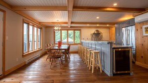 A spacious kitchen with wooden floors, a central island with stools, and a large window overlooking greenery.