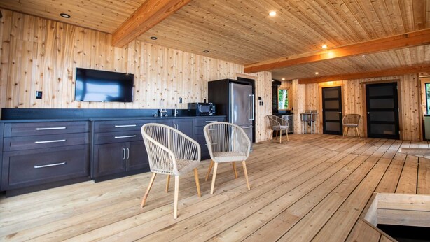 A spacious kitchen with wooden walls, a large TV, and a dining area with wicker chairs.