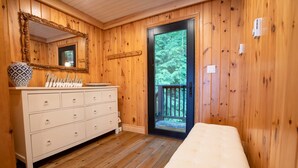 A room with wooden walls, a white dresser with drawers, a large mirror, and a door leading outside.