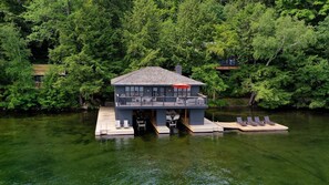 Une péniche dotée d’un balcon, amarrée sur une rivière paisible, entourée d’une forêt dense.