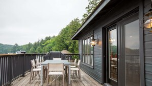 A wooden deck with a table and chairs, overlooking a forested area.