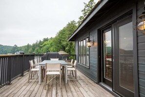 Eine Terrasse mit Tisch und Stühlen, einem Grill und Blick auf einen bewaldeten Bereich.