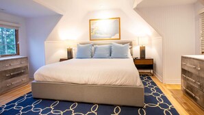A bedroom with a large bed, two bedside tables with lamps, a dresser, and a window with blinds.