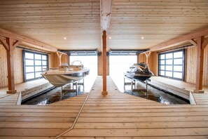 Eine Holzdiele mit einem offenen zentralen Bereich, zwei Booten, die an den Seiten festgemacht sind, und Blick auf das Wasser durch große Fenster.