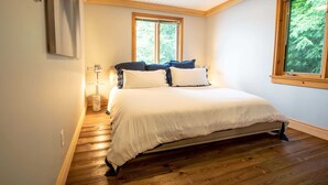 A bedroom with a bed, a nightstand, a lamp, and a window with a view of trees.