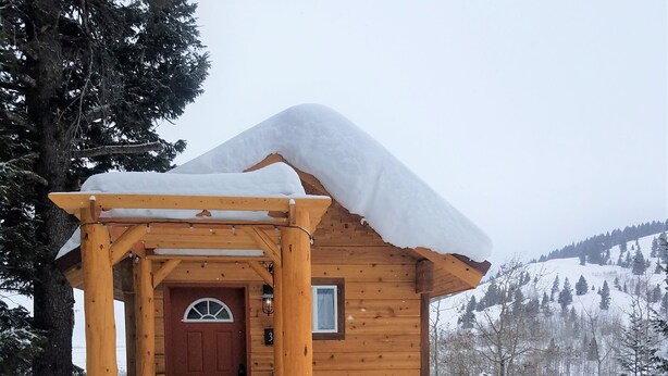 Een houten hutje met een sneeuw bedekte ingang en een houten veranda.