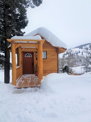 Une cabane en bois, dont l’entrée et le porche sont recouverts de neige.