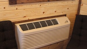 Een witte, draagbare airconditioner in een kamer met houten lambrisering en twee donkergrijze fauteuils.